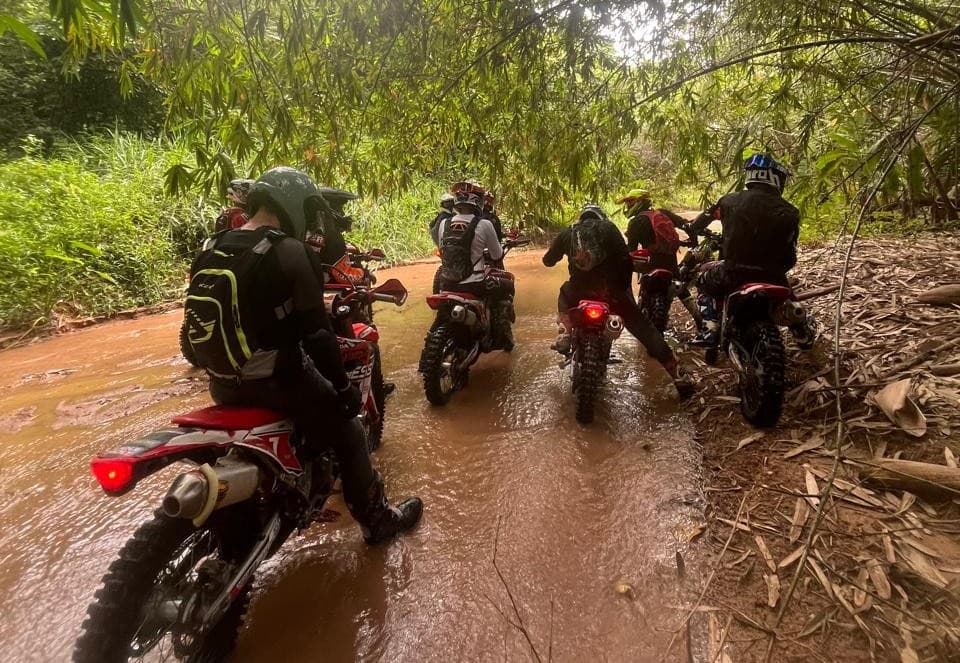 Group crossing muddy river on dirt bikes through Thai jungle